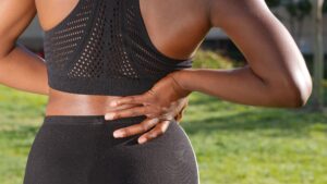 Woman in athletic attire holding her back outside, indicating discomfort or pain.