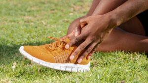 Person holding ankle in orange sneaker, suggesting potential sports injury.
