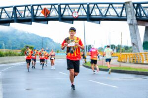 Marathon runners in colorful shirts race under a bridge on a city street.
